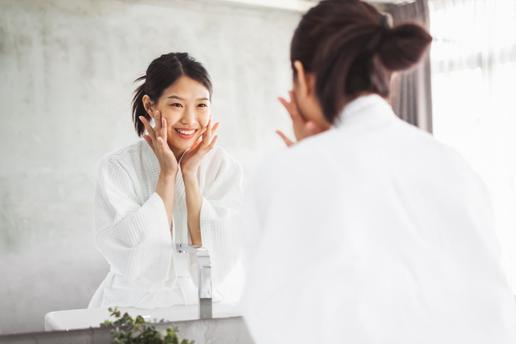 Asian woman cleaning face front of mirror, skin care and cosmetic removal concept