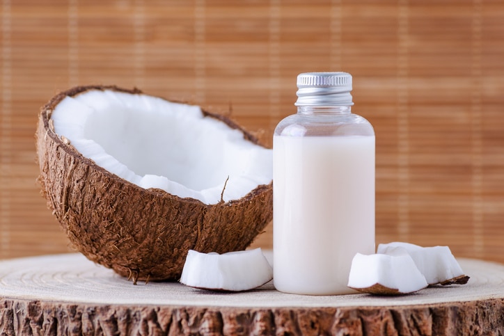 cosmetic bottle and fresh organic coconut for skincare, natural brown background