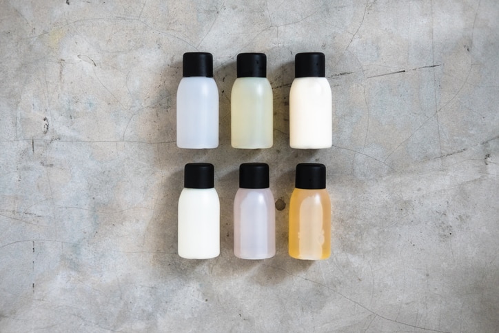 Travel-sized mini bottles cosmetic products from above on concrete table. Skincare, moisturizers, essences, body and hair treatments. Minimalism blogging concept.