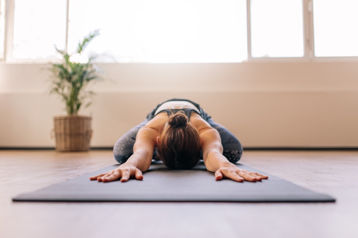 Fit woman performing child yoga pose at gym class. Fitness woman working out on yoga mat indoors.