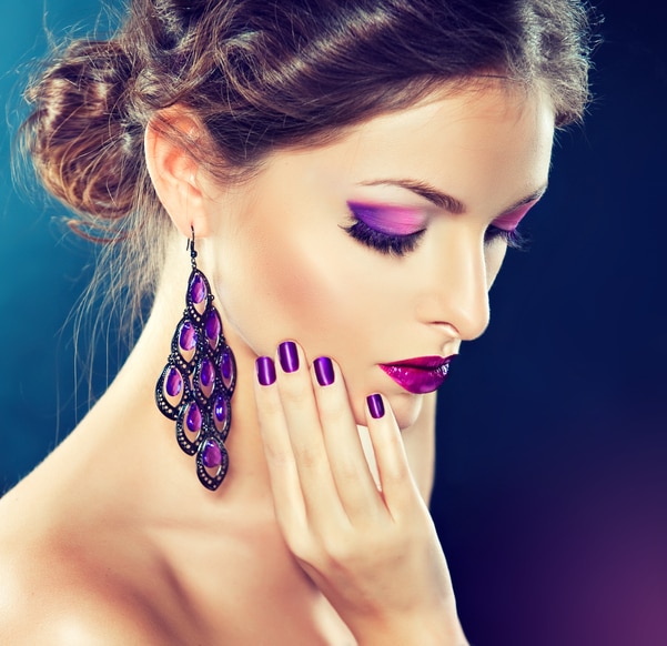 Bright stylish make up and manicure in a purple colore. Close up portrait young woman dressed in a  big oriental-style earings. Jewelry and cosmetic, large violet earrings.