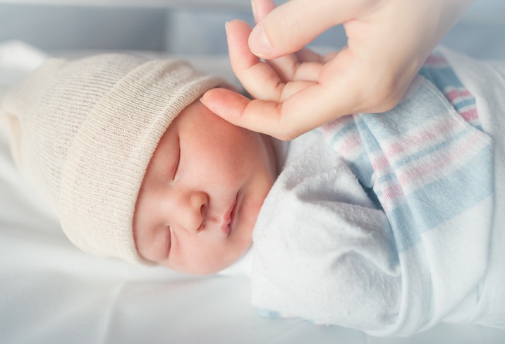 Mothers hand comforting new born baby boy sleeping.