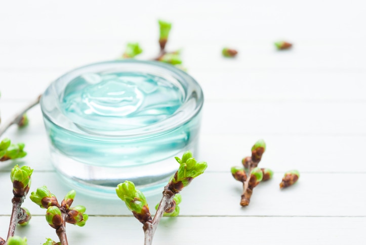 blue beauty product gel and leaf buds on white wood table