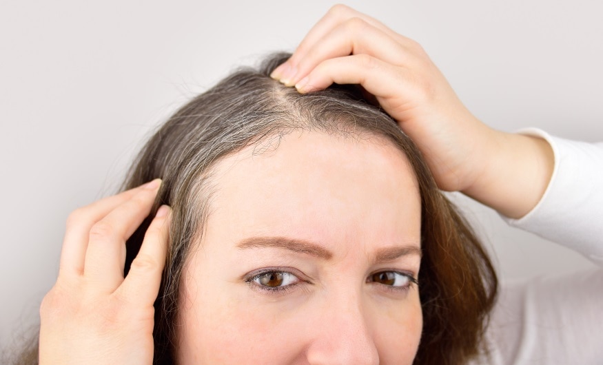 woman is checking white hair while looking at the mirror