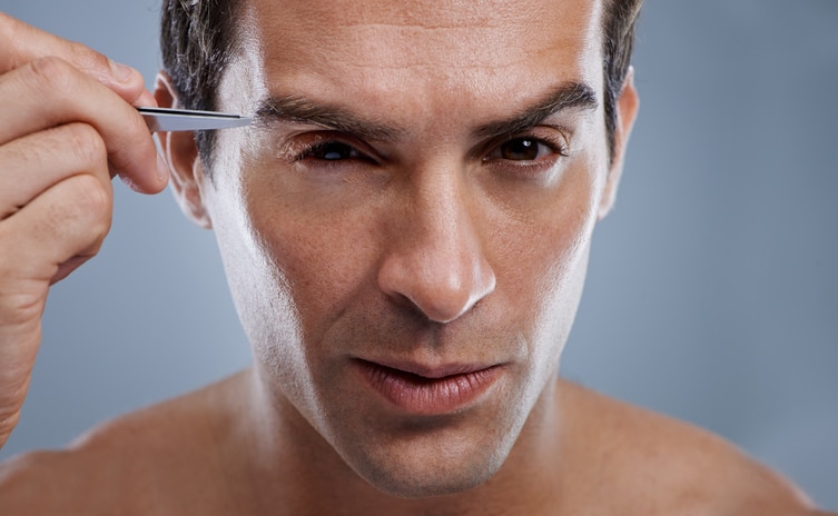 A young man tweezing the hair on his face