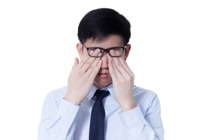 Young Asian businessman rubbing his tired eyes from long hours of works using computer