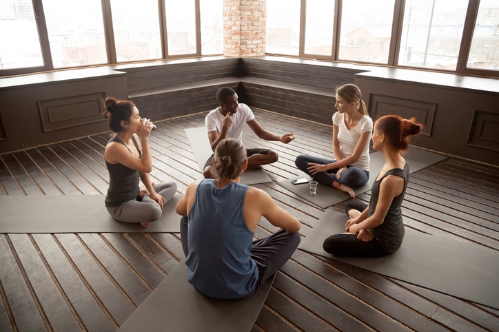 African american yoga instructor talking to diverse group sitting on mat in studio, multiracial happy people having conversation about healthy mindful life and motivation at training seminar class