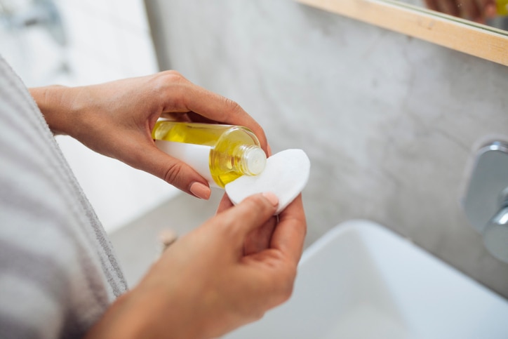 Woman standing in bathroom and putting cosmetic oil on cotton pad.