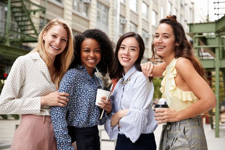 Four female coworkers smiling to camera outside