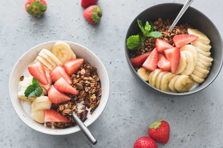 Granola with banana, strawberry and yogurt in bowl on gray concrete background. Top view. Healthy eating, healthy breakfast, fitness menu