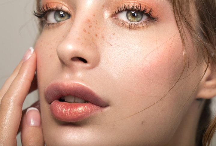 Closeup studio shot of a beautiful young woman with freckles skin posing against a grey background