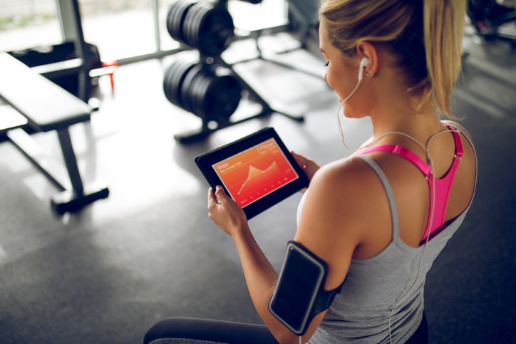 Young woman tracking her progress with a fitness app on digital tablet at gym