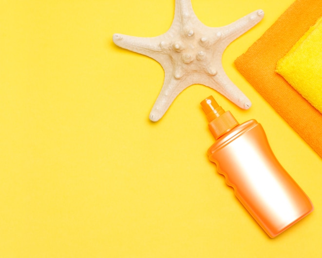 Bottle of sunscreen spray with starfish and towels. Suntan lotion. Copy space