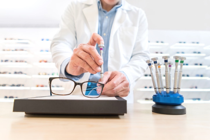 Man repairing glasses at the optics using a screwdriver - healthcare and medicine