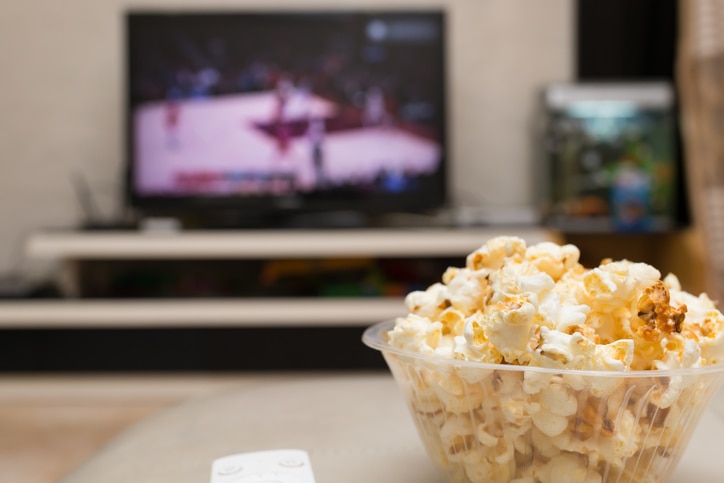 popcorn and remote control on sofa with a TV broadcasting basketball match on background