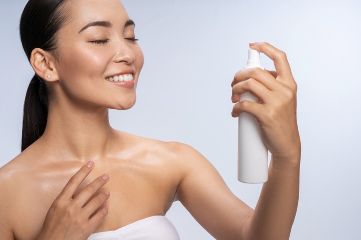 Woman spraying facial mist on her face, summertime skincare concept