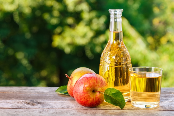 apple cider or juice in glass with ripe fresh apples on wooden table with green natural background. Horizontal shot. Summer drink