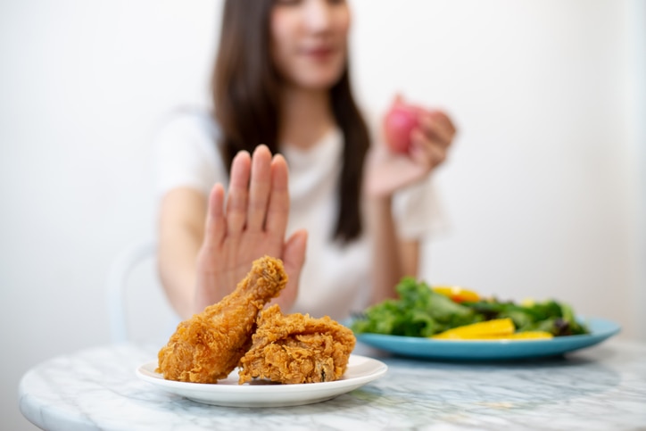 Dieting or good health concept. Young woman rejecting Junk food or unhealthy food such as fried chicken or dessert and choosing healthy food such as fresh fruit or vegetable.