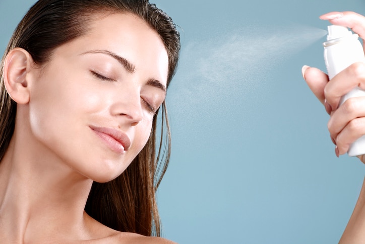 Beautiful woman applying spray  water treatment on face on blue background