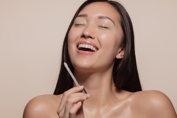 Young woman smiling with her eyes closed while doing makeup. Korean female model enjoying doing make up.