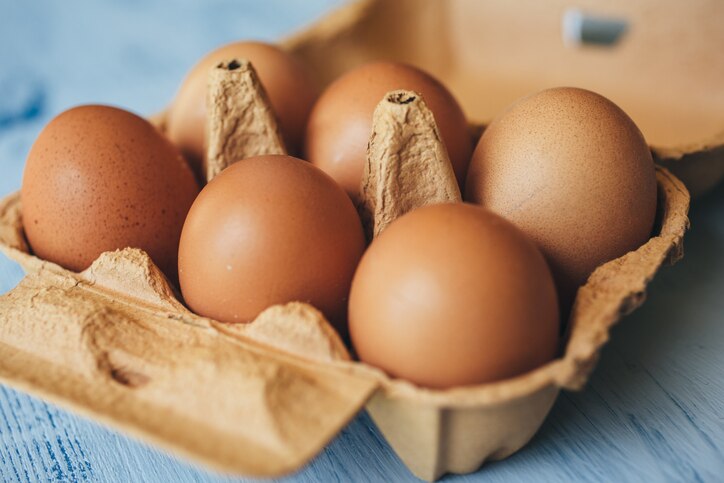 Eggs background. Closeup view of eggs in carton box on wooden table. Food and health concept.