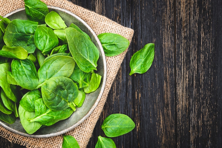 Green spinach leaves in bowl on rustic wooden table. Top View