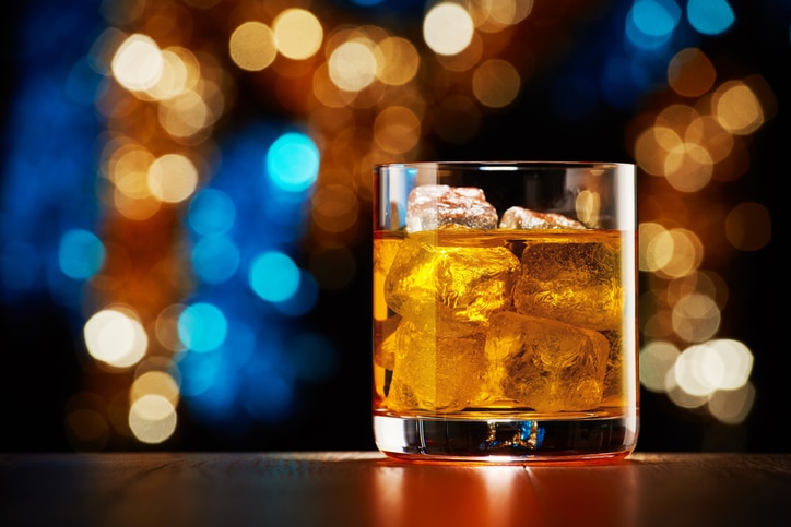 Glass of whiskey with ice on colorful Christmas lights bokeh background