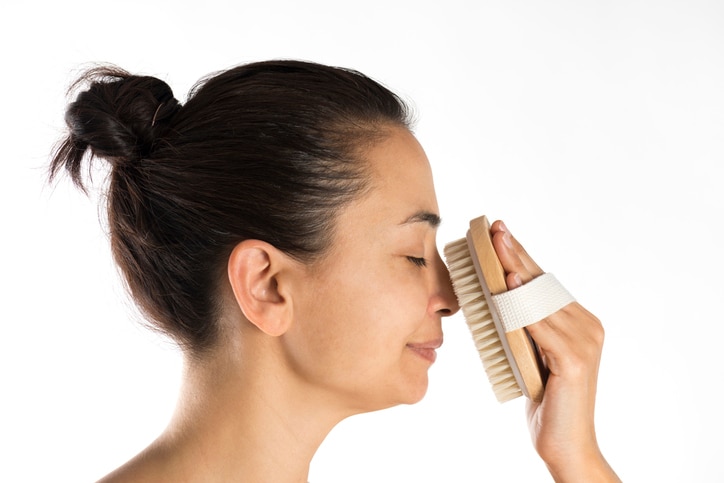 Woman scrubbing her face with a scrubbing brush.