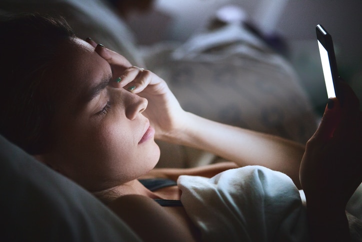 Tired woman in bed with smartphone, low light