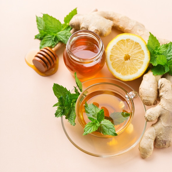 Warm drink beverage infusion in glass for cold flu winter fall days. Cup of ginger tea with mint, lemon and honey on a coral table. Copy space, flat lay background