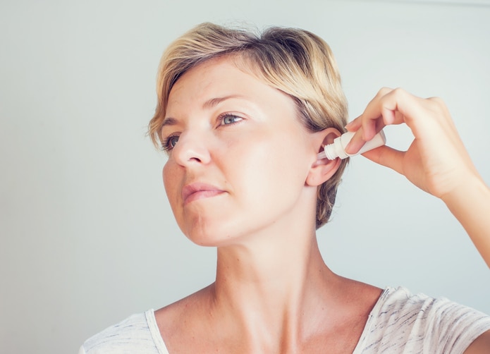 woman using ear drops on gray background