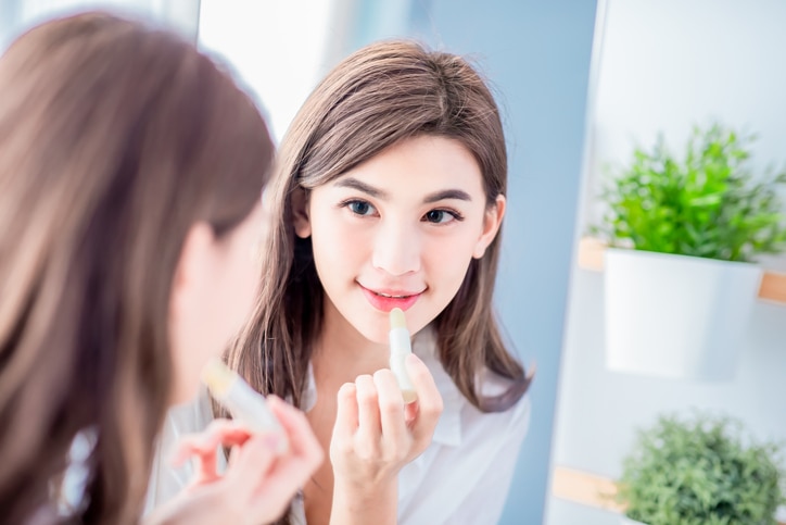 beauty woman applying lip balm and looking at mirror