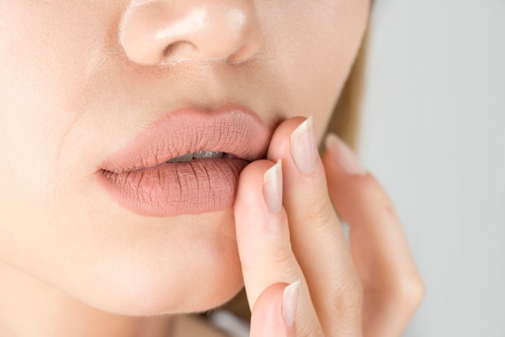 Caucasian female is touching her lips because of herpes pain.