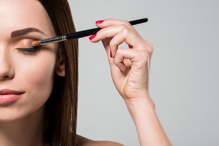 young beautiful woman applying eyeshadows isolated on grey