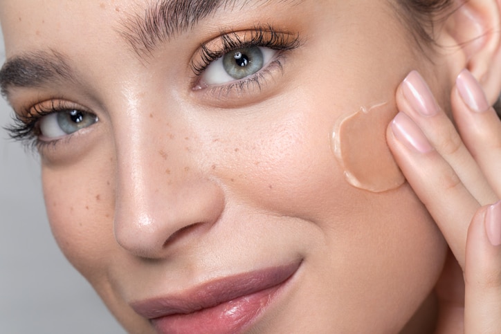 Close up studio shot of a beautiful woman with perfect freckled skin, applying foundation.