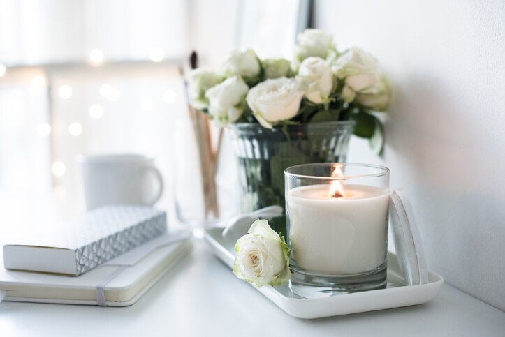 White room interior decor with burning hand-made candle and bouquet of fresh roses on table, luxury home decorations in daylight closeup