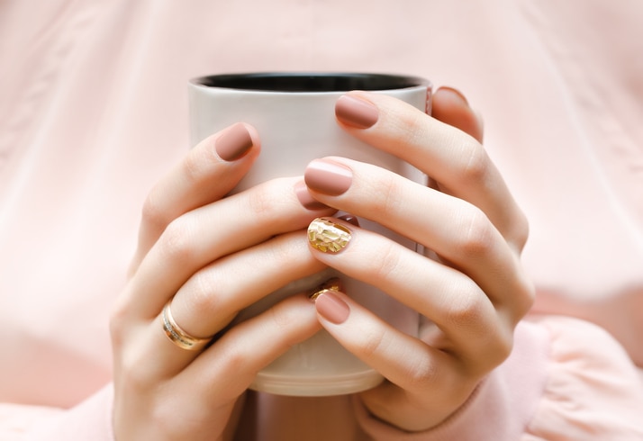 Female hands with beige nail design holding white cup.