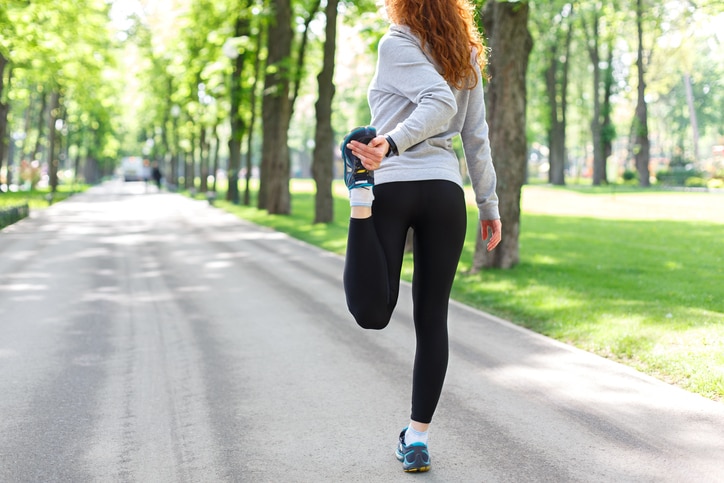 Young female runner warming up before running at morning park, back view