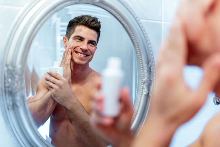 Healthy positive male treating sking with lotion after shaving