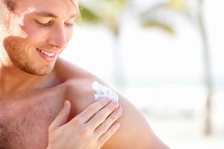 Solar cream / sunscreen. Man putting sunblock sun screen cream on the beach under the sun during vacation on travel resort. Young caucasian male model.