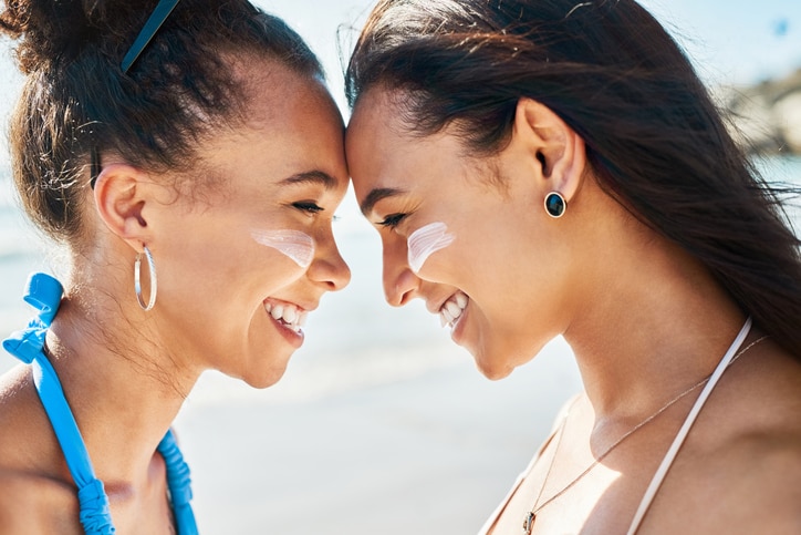 Shot of two beautiful young women at the beach with sunscreen on their faces smiling at each other