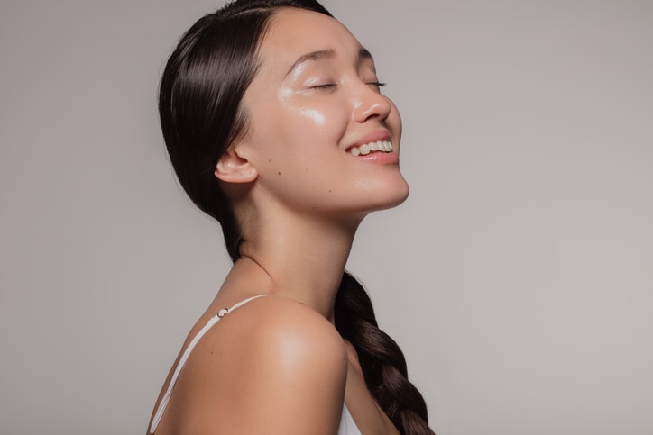 Asian woman with beautiful and healthy skin on beige background. Girl smiling with her eyes closed.