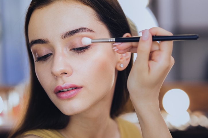 Eye shadows. Gorgeous good-looking woman using her eye shadows while holding little face brush in her hand