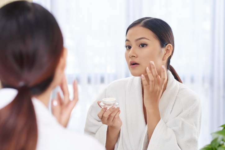 Beautiful young woman applying anti-aging cream on her face