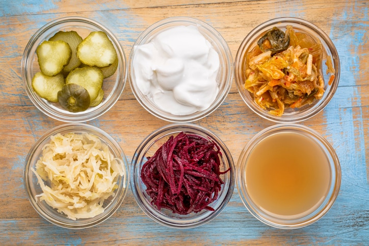 a set of fermented food great for gut health - top view of glass bowls against grunge wood:  cucumber pickles,  coconut milk yogurt, kimchi, sauerkraut, red beets, apple cider vinegar