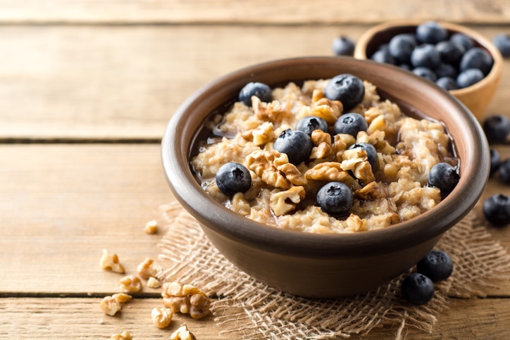 Oatmeal porridge with blueberries, walnuts and honey in ceramic bowl on wooden background. Rustic style. Selective focus.