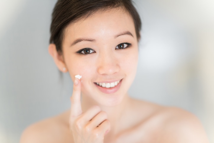 Asian woman applying cream in her face