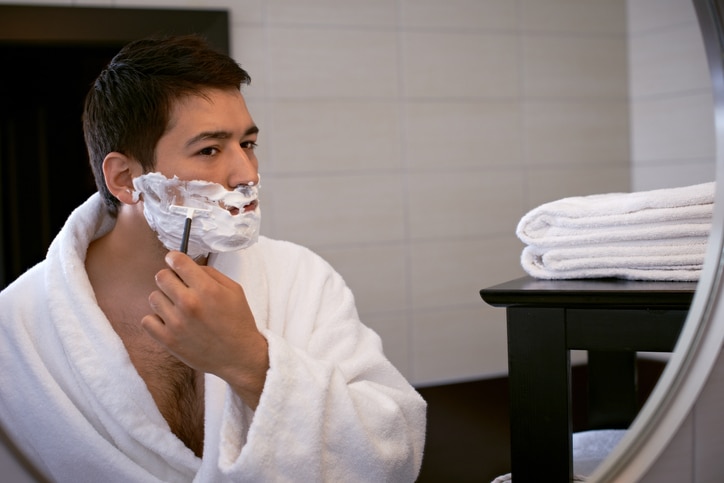 Young man shaving in front of a bathroom mirror