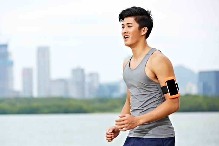 young asian male jogger with fitness tracker attached to arm running with skyline in the background.