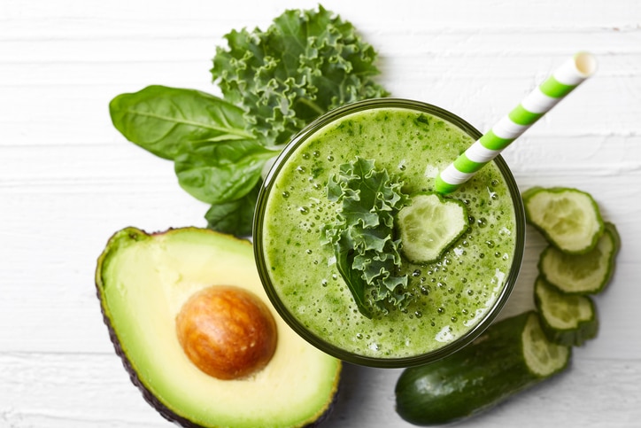 Glass of green vegetable smoothie on white wooden background from top view